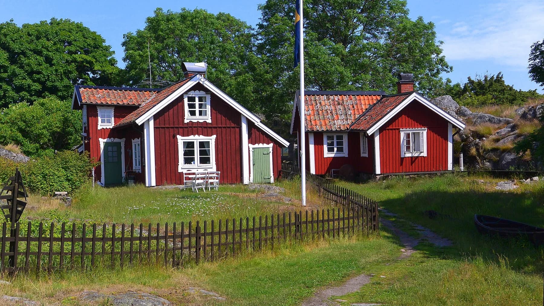 Röda skärgårdshus mellan grönska och klippor vid Hemviken på Bullerö