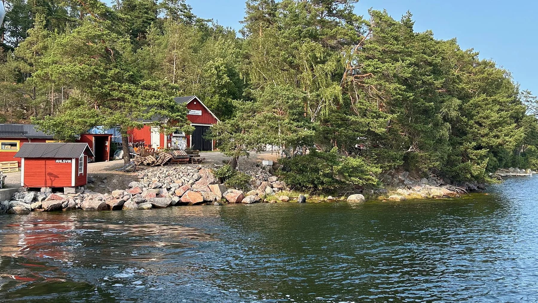 Röda sjöbodar och klippig strand vid Alsvik på Svartsö