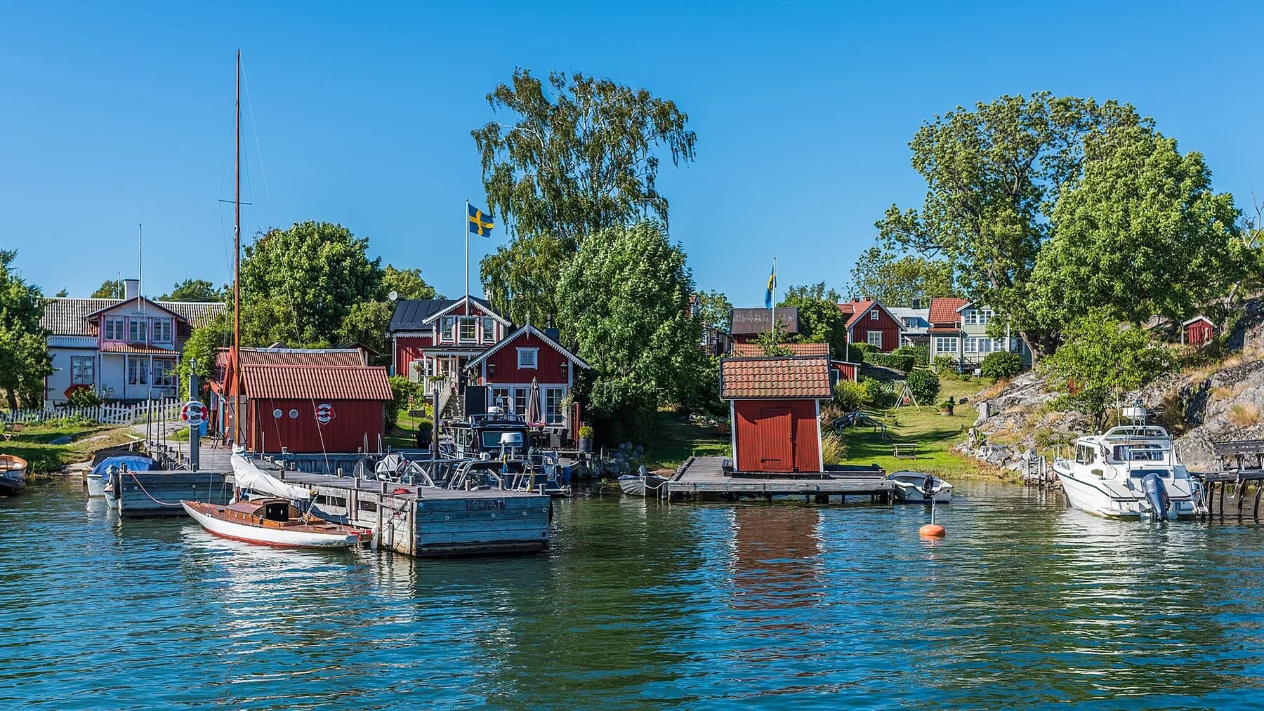 Färgstarka skärgårdshus och båtar i en skyddad vik på Möja
